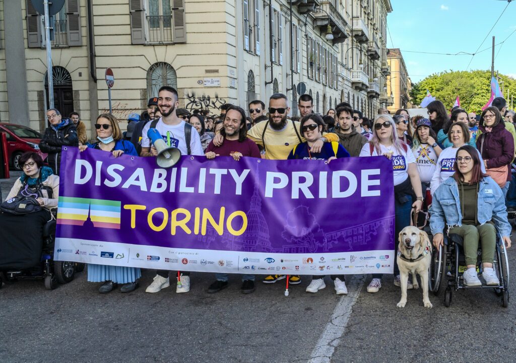 Persone disabili motorie e sensoriali e persone non disabili dietro allo striscione del Disability Pride Torino in occasione dell'edizione 2024